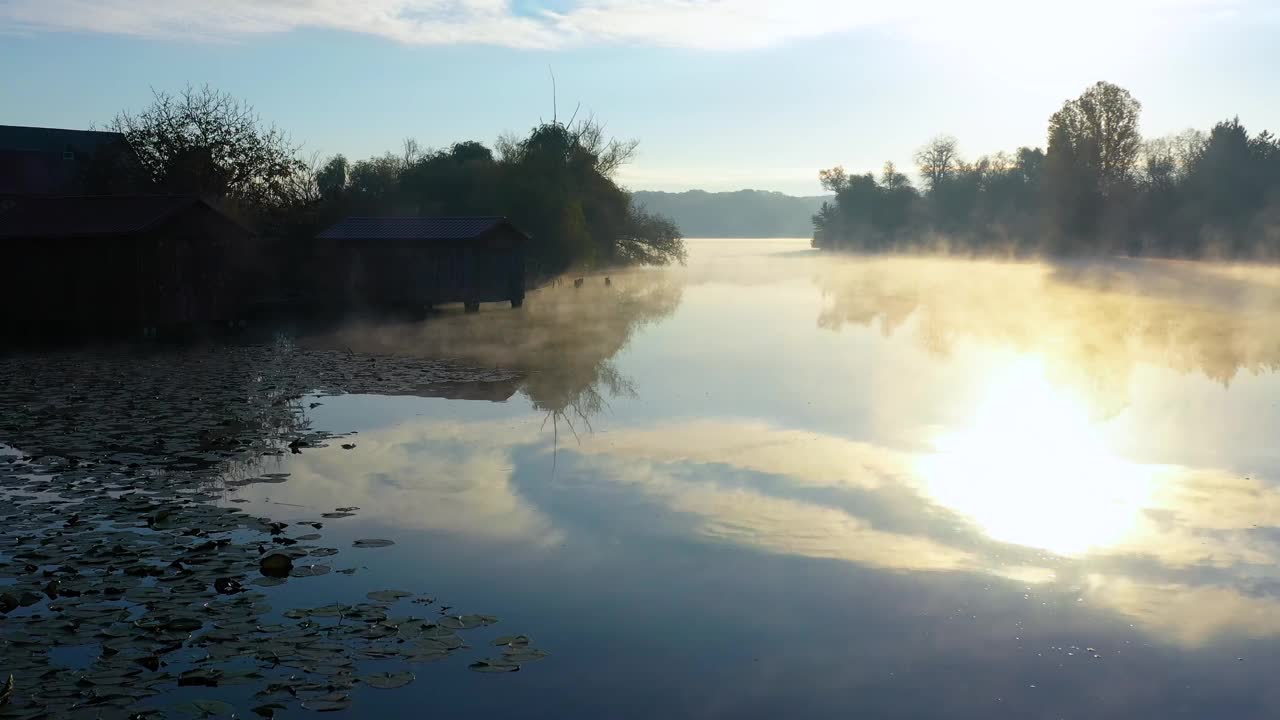 湖上的晨雾与远处的森林。薄雾飘浮在平静的湖面上。鸟瞰图缓慢漂浮的蒸汽，蒸汽在湖上钓鱼的房子。平静的水面反射着云朵。视频素材