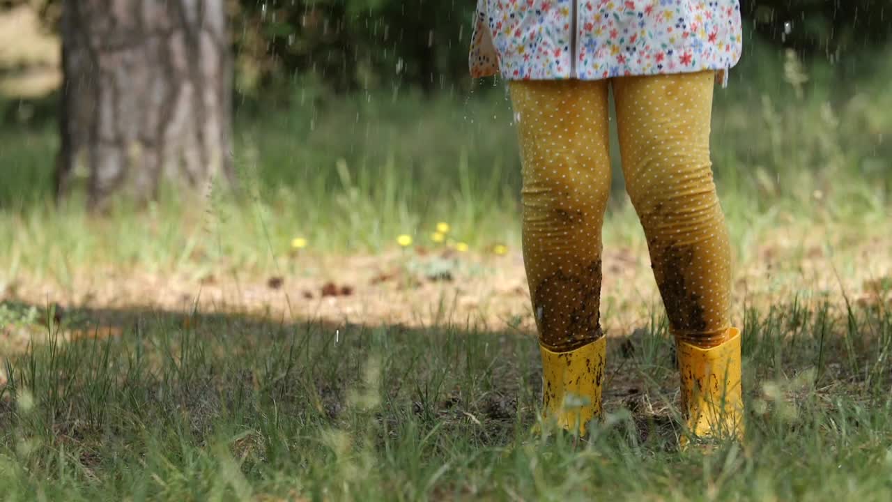 夏天的雨中，穿着黄色靴子的女孩在水坑上跳跃视频素材