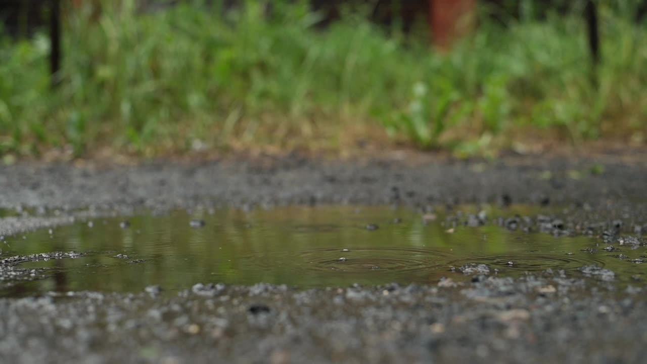 一个穿着黄色胶靴的孩子在雨中的水坑里奔跑玩耍视频素材