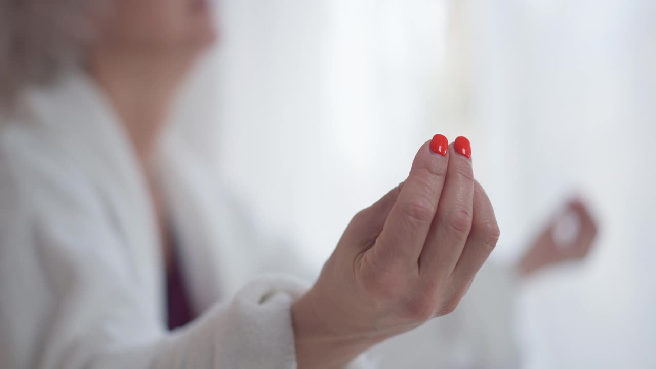 特写的手模糊不认识的成熟女人冥想坐在莲花的姿势在室内。集中的白人女性瑜伽修行者在家练习。舒适宁静的概念。视频素材