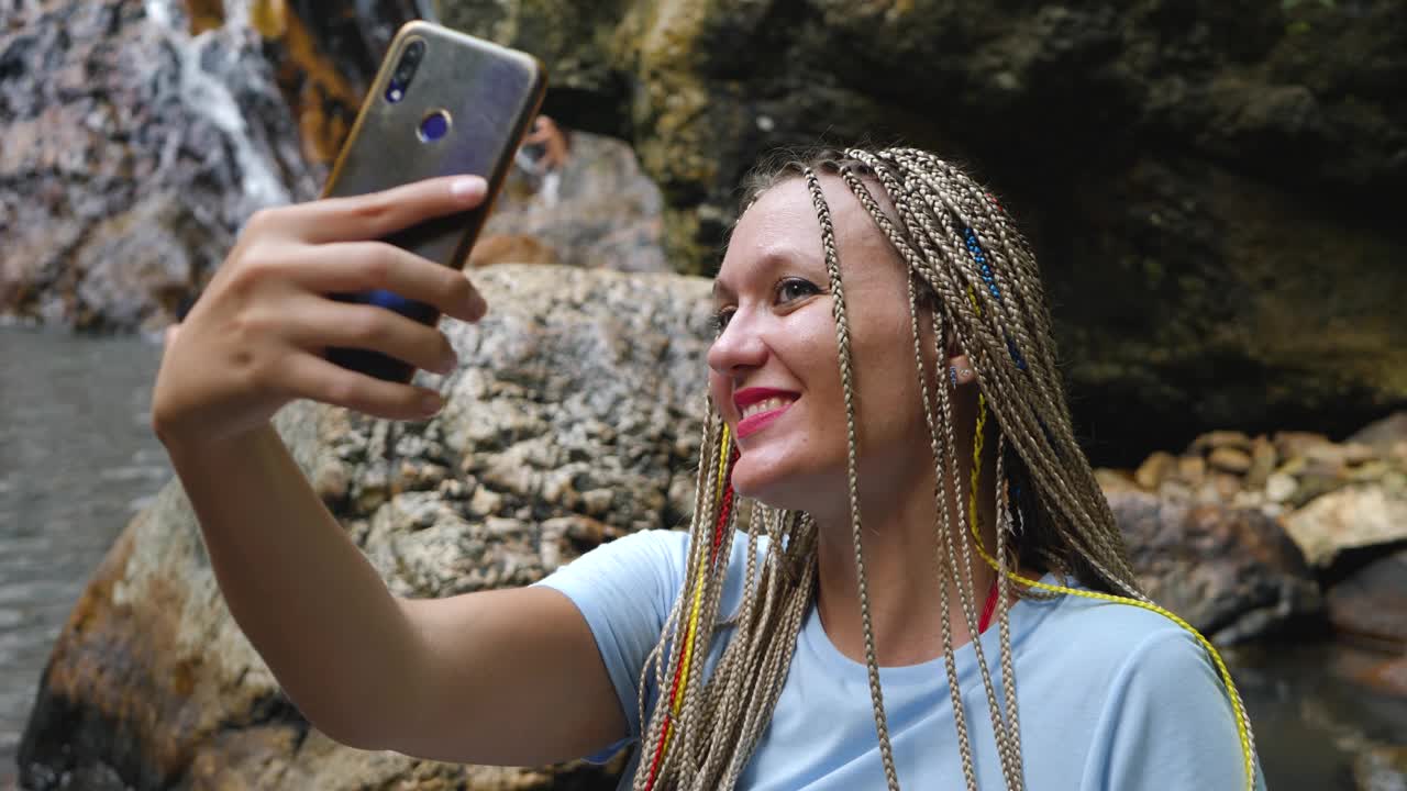 女旅行者站在山上瀑布溪流旁为博客拍照视频素材