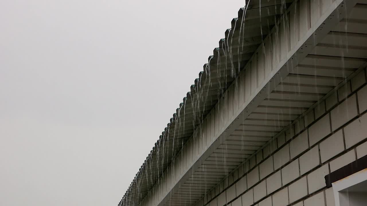 多雨气候主题。一股雨水从一栋砖砌的独栋房屋的屋顶流下来。夏天多云的天空下着大雨。有选择性的重点视频素材