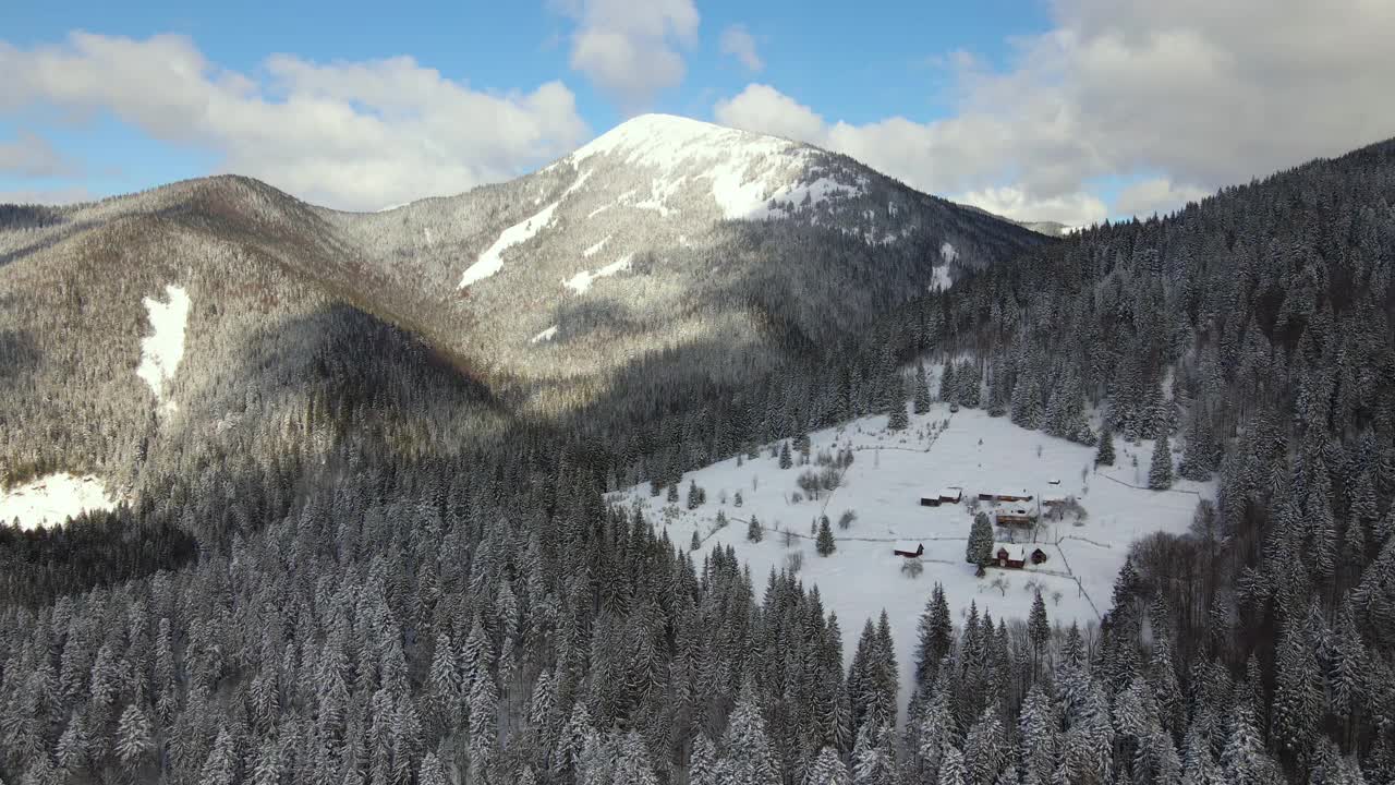 空中冬季景观与小乡村房屋之间的雪覆盖森林在寒冷的山。视频素材