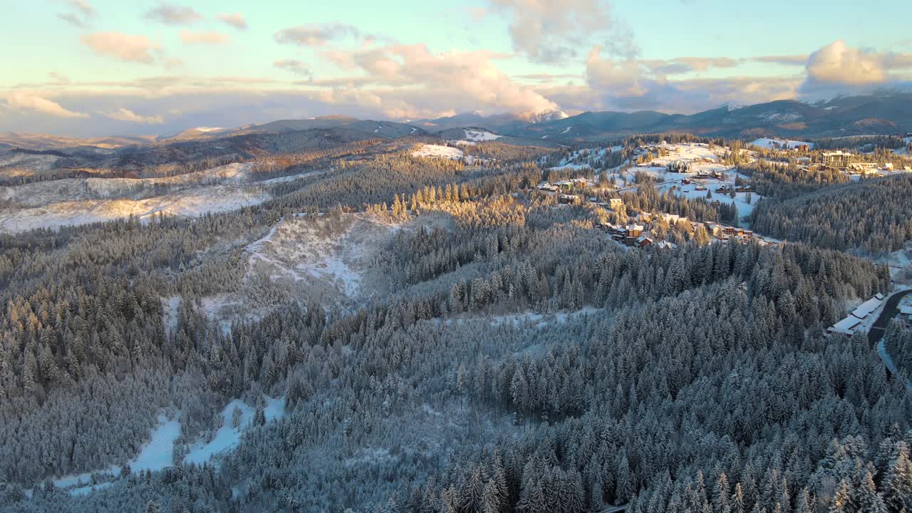 空中冬季景观与小村庄房屋之间的雪覆盖森林在寒冷的山在晚上视频素材