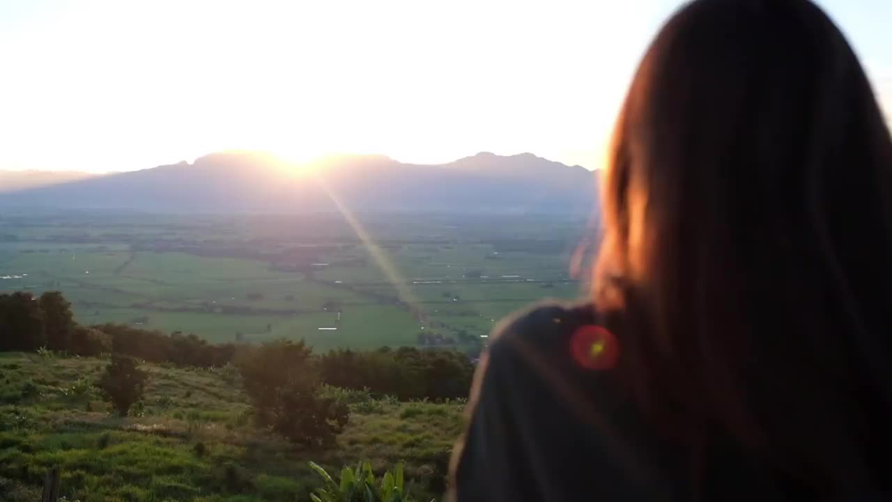 一个年轻女人在傍晚看日落和山景的慢动作视频素材