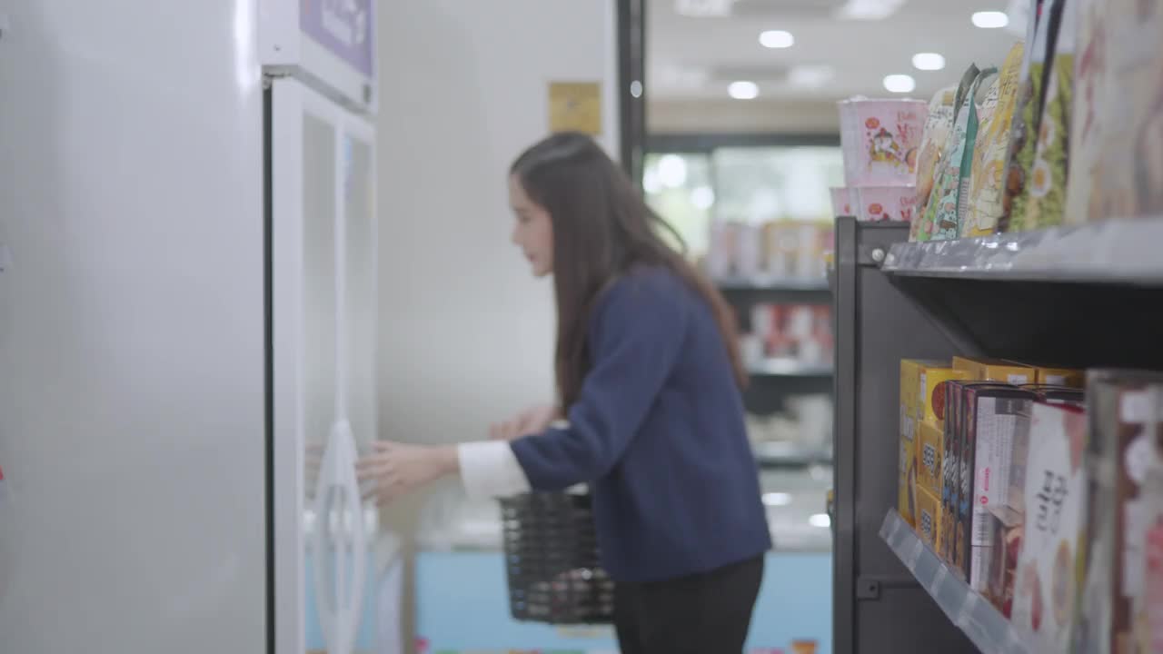 一位妇女在冰箱里选择饮用水，一位亚洲女商人穿着蓝色的休闲装正在购买商品和服务视频素材