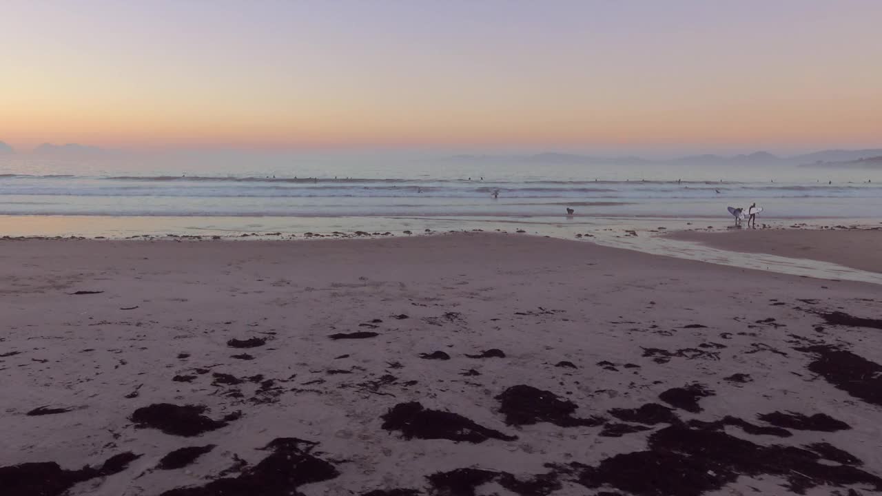 鸟瞰图，波在帕托斯海滩打破，人们在金色的日落和山的背景，加利西亚，西班牙。多莉离开。视频下载