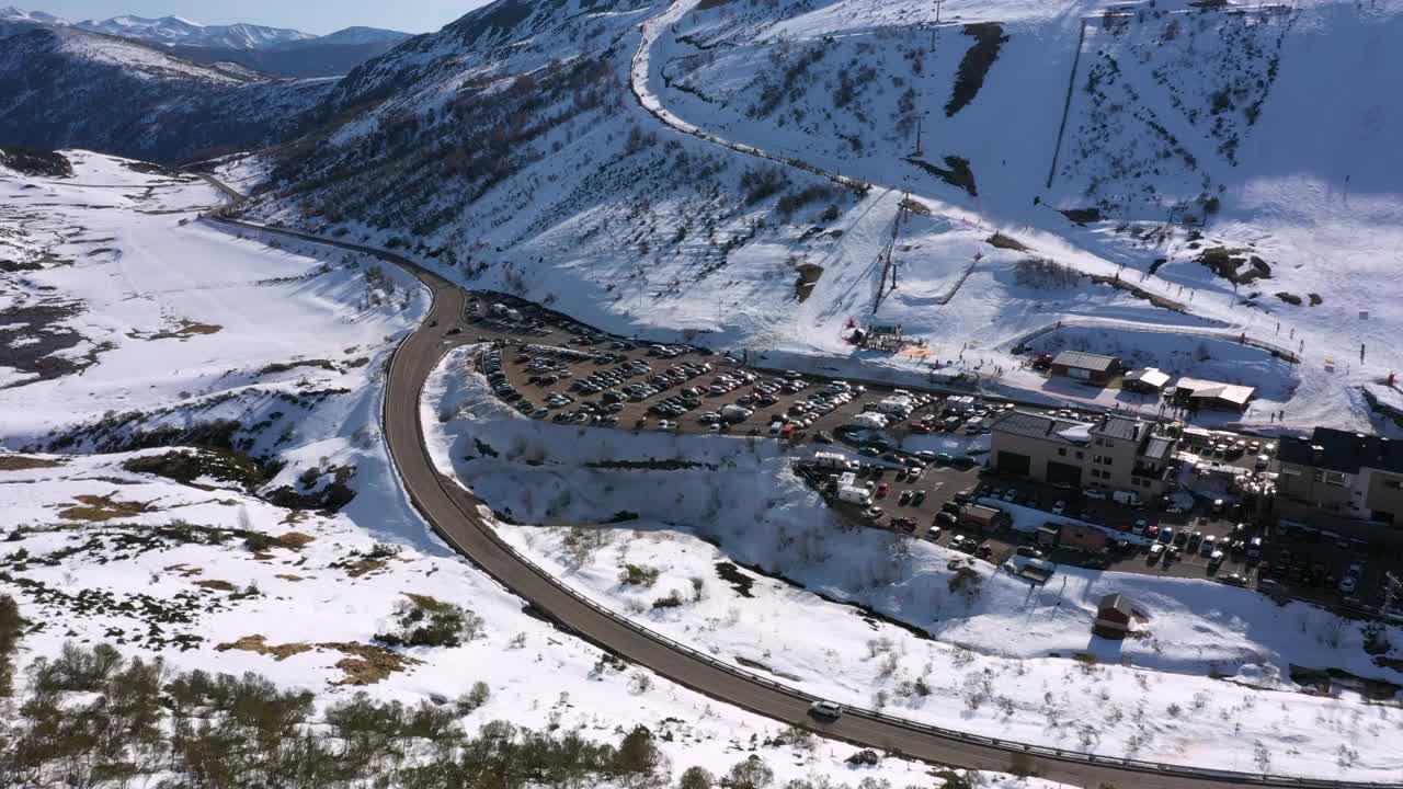 空中，跟踪，无人机拍摄的Leitariegos滑雪场，在一个阳光明媚的日子，在西班牙莱昂，一个停车场，满是汽车，酒店和在山上滑雪的人视频素材