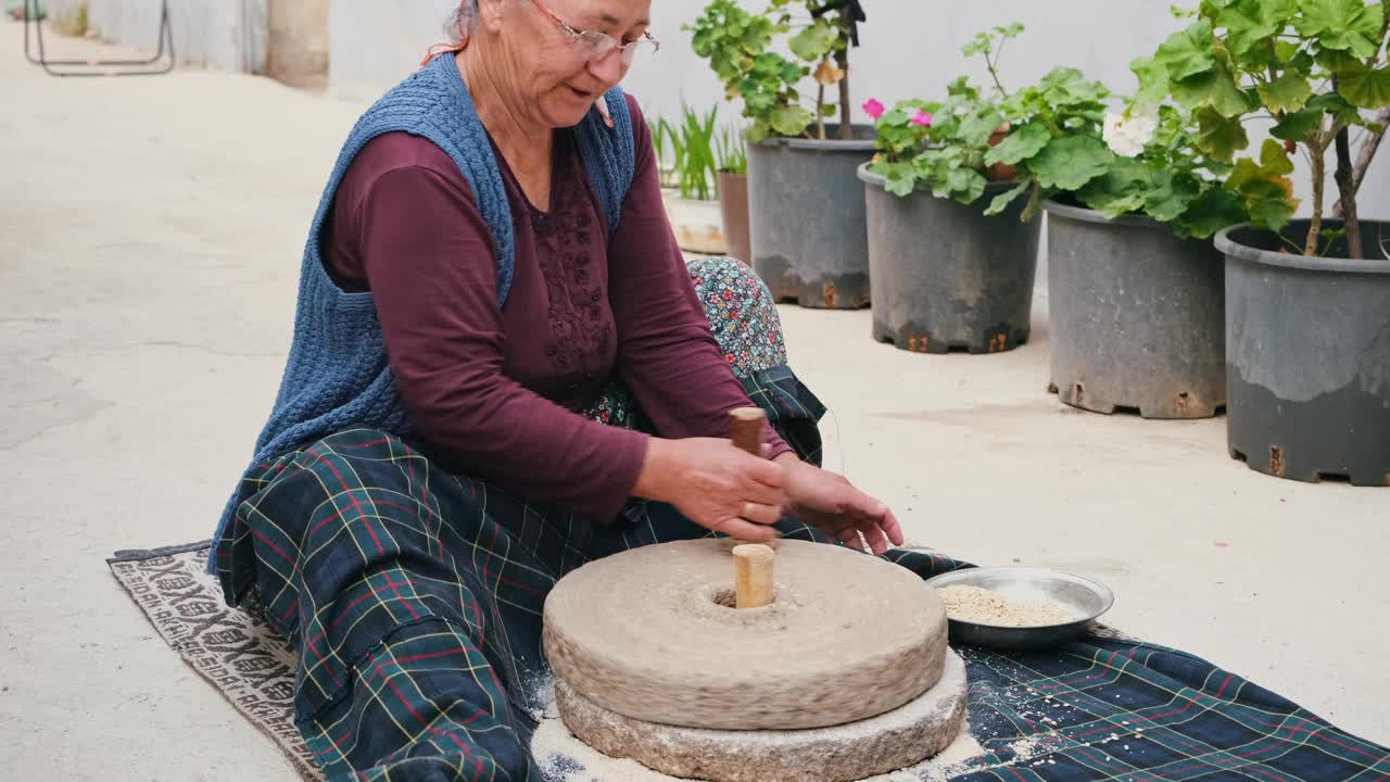 那位老妇人正在用古老的传统方法在石磨里磨面粉。磨粉机用于将小麦磨成面粉，传统的磨粉生产。视频素材