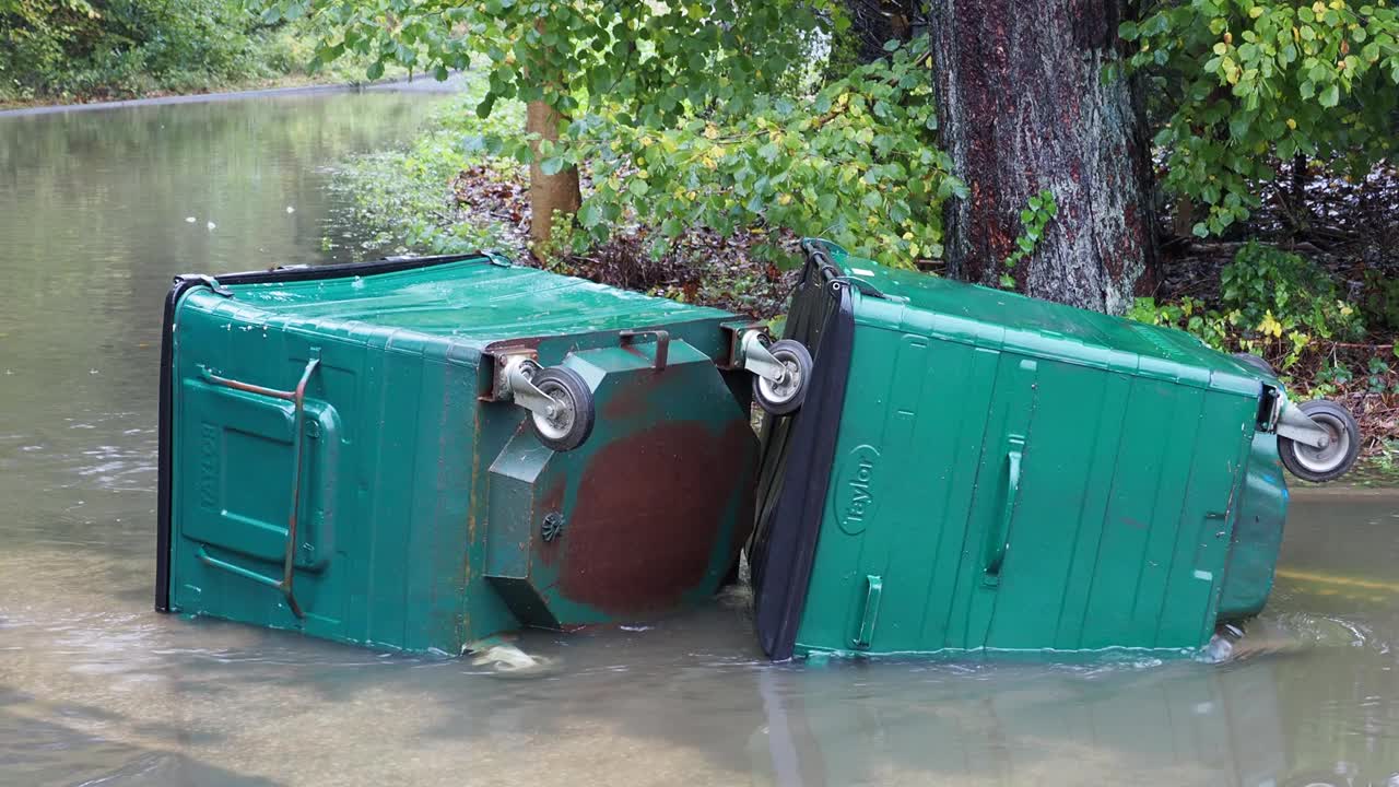 在英国湖区安布尔赛德的一条被洪水淹没的道路上，暴雨导致罗赛河决堤，有轮子的垃圾桶被洪水冲到道路上。视频素材