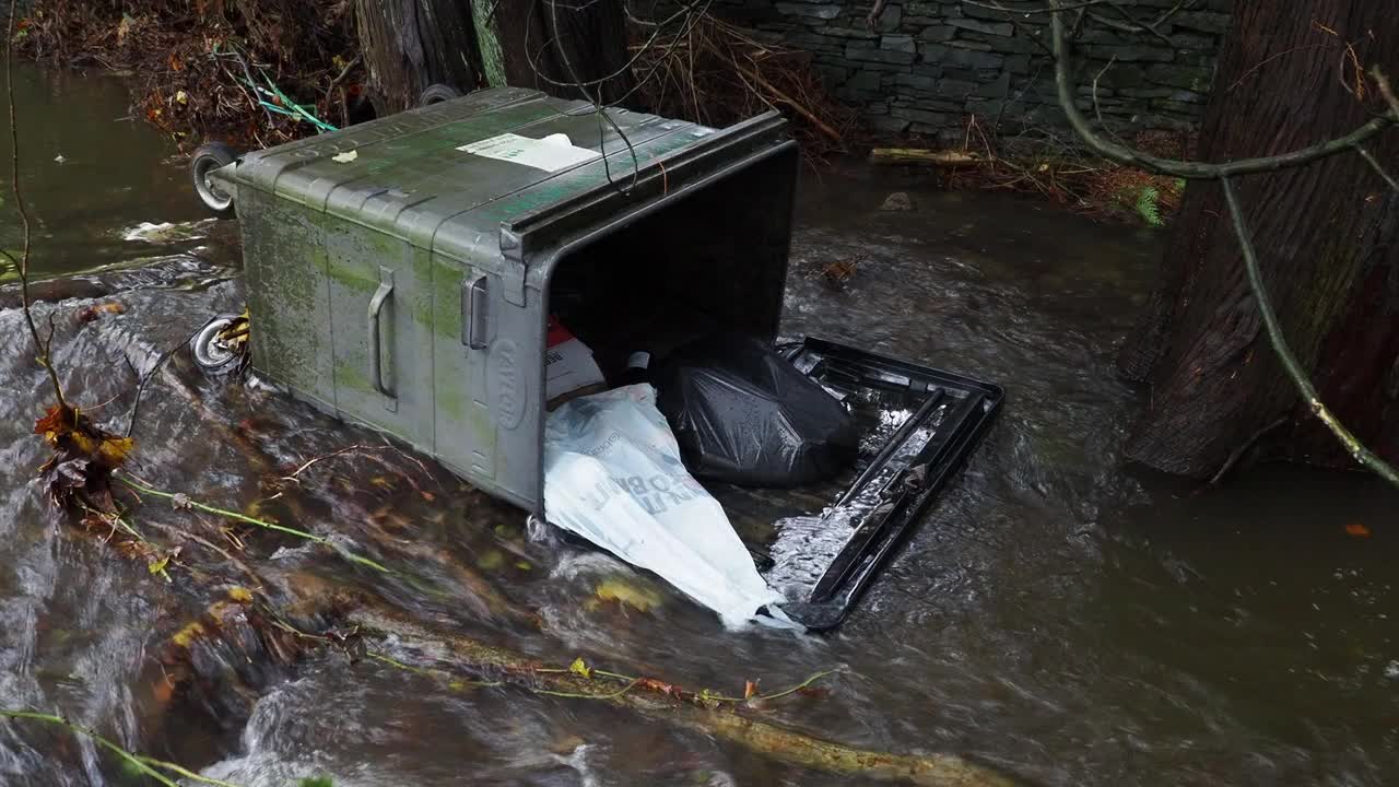 在英国湖区安布尔赛德的一条被洪水淹没的道路上，暴雨导致罗赛河决堤，有轮子的垃圾桶被洪水冲到道路上。视频素材