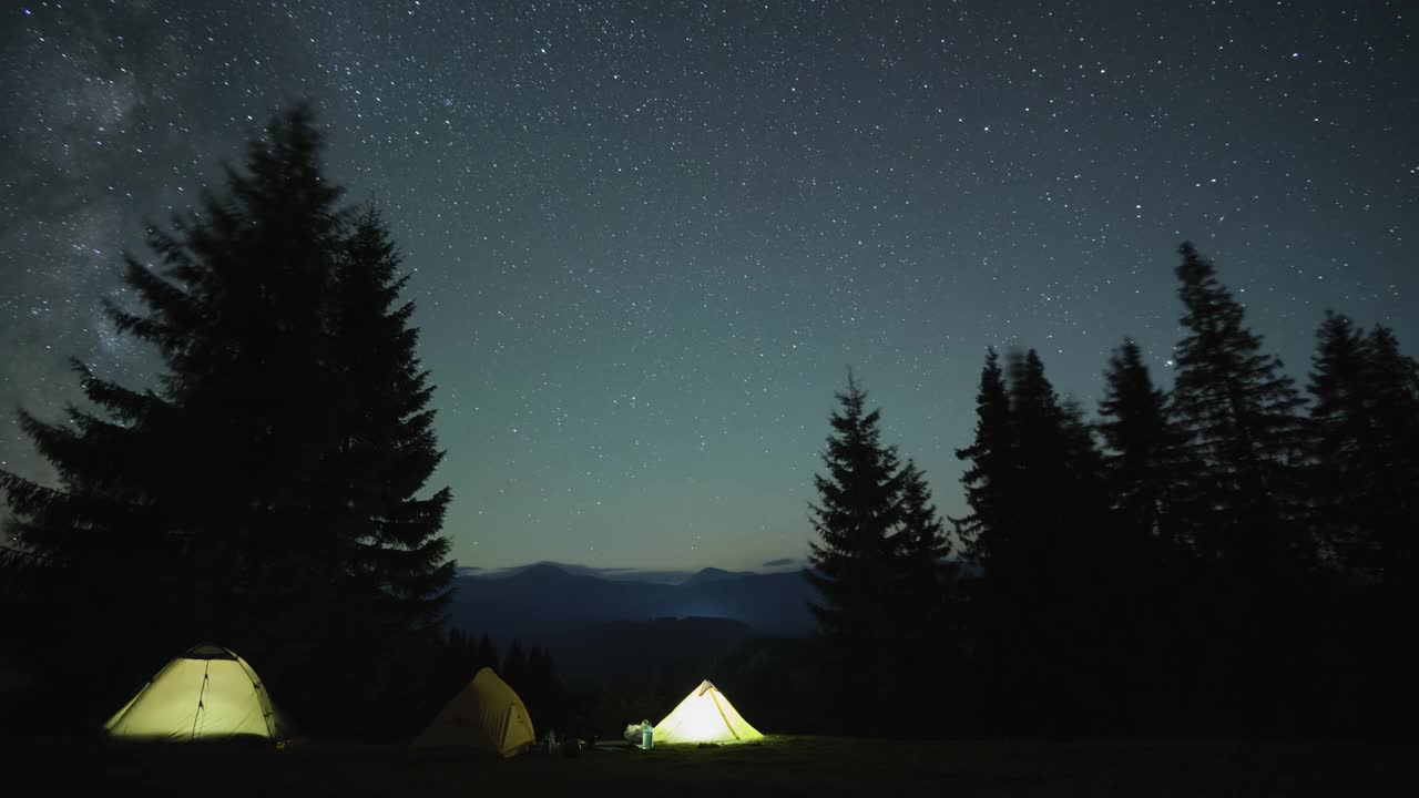 在星星闪烁的夜空下，山间树林中露营地的游客帐篷旁，明亮的篝火旁，徒步旅行者在休息。积极的生活方式和户外生活理念视频素材