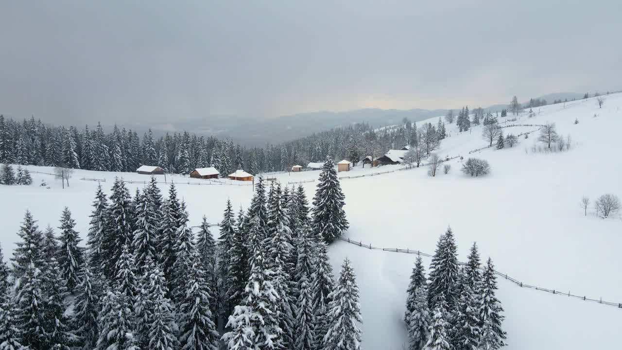 空中冬季景观与小乡村房屋之间的雪覆盖森林在寒冷的山视频素材