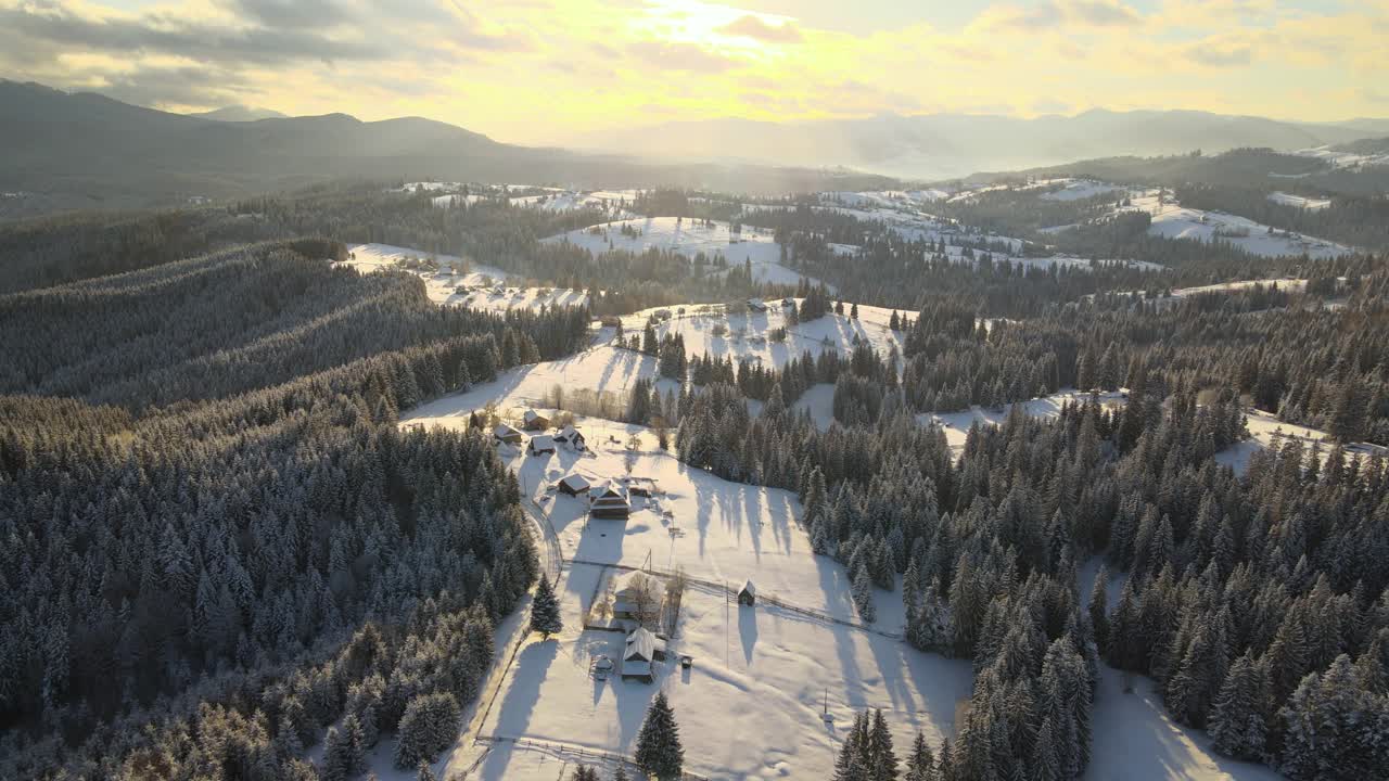 空中冬季景观与小村庄房屋之间的雪覆盖森林在寒冷的山在晚上视频素材