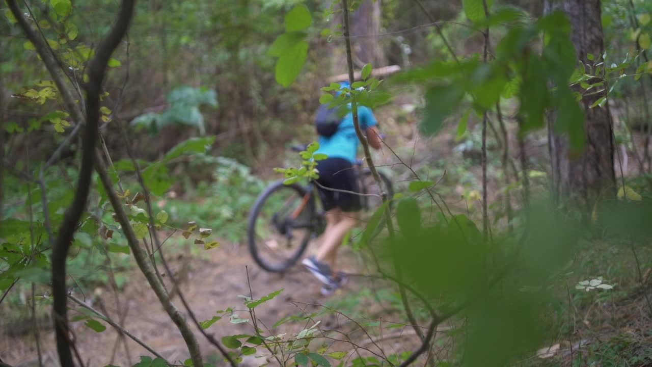 年轻的山地车手推着山地车在森林里上坡视频素材