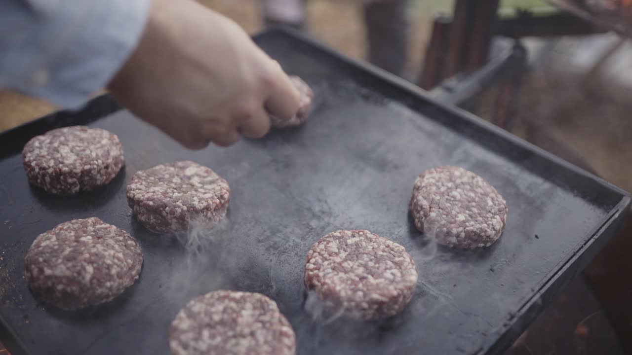 近距离的手放置牛肉汉堡在一个石头板上的木材烧烤视频素材