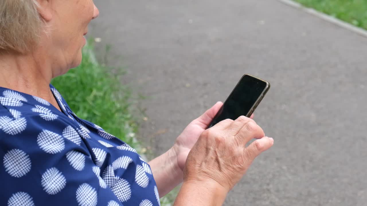 高级女性手持智能手机的特写镜头。现代退休老年女性使用无线网络，视频素材