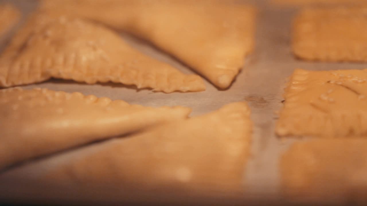 生的酥皮馅饼撒上芝麻，放在铺上羊皮纸的烤盘上，放在烤箱里烤。烹饪烘焙的过程视频素材