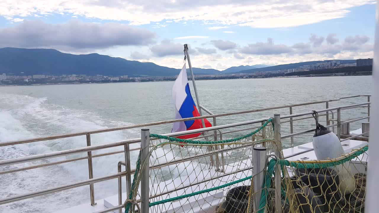 船上的俄罗斯国旗在风中飘扬，以黑海为背景，以格连兹克的海岸线为背景视频素材