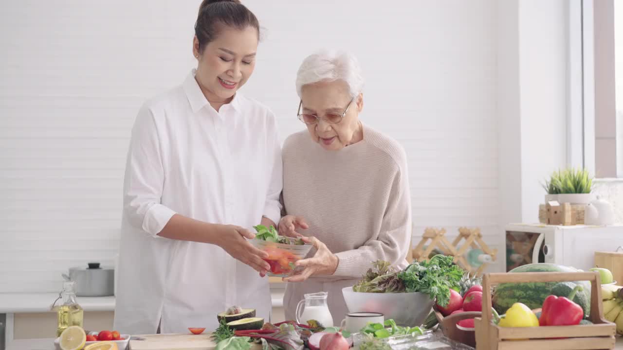 亚洲资深母亲选择什么蔬菜她可以吃，与中间的女儿在厨房准备健康的早餐，蔬菜，水果，享受周末活动，前面的视图视频素材