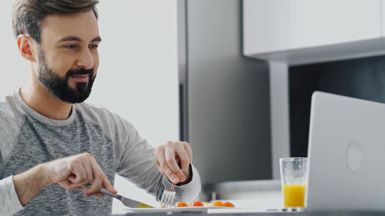 近景:微笑的大胡子男人在吃晚饭，用笔记本电脑视频素材