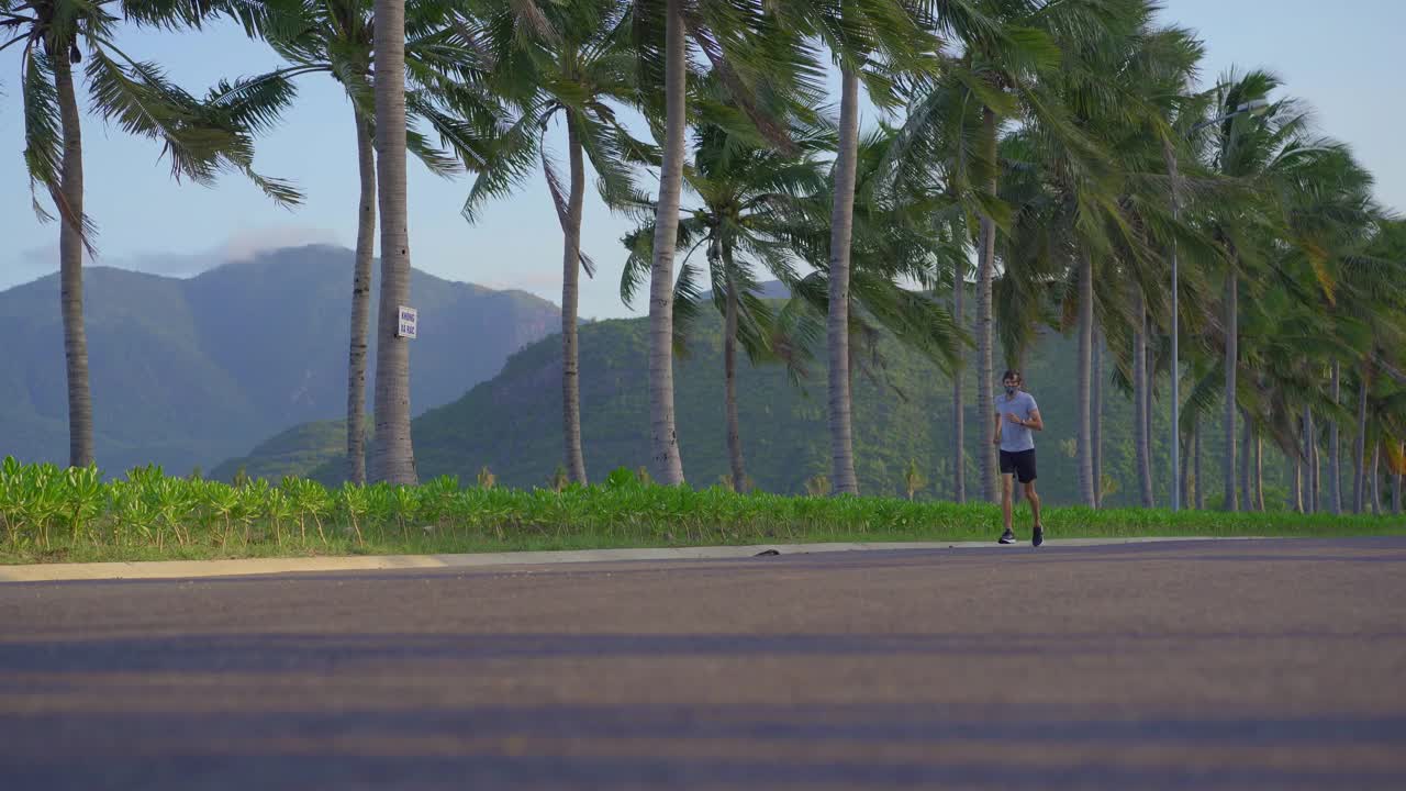 在热带地区的街道上，一名戴着口罩的男子正在奔跑。视频素材