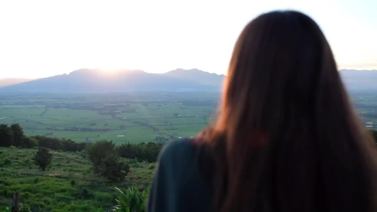 一个年轻女人在傍晚看日落和山景的慢动作视频素材