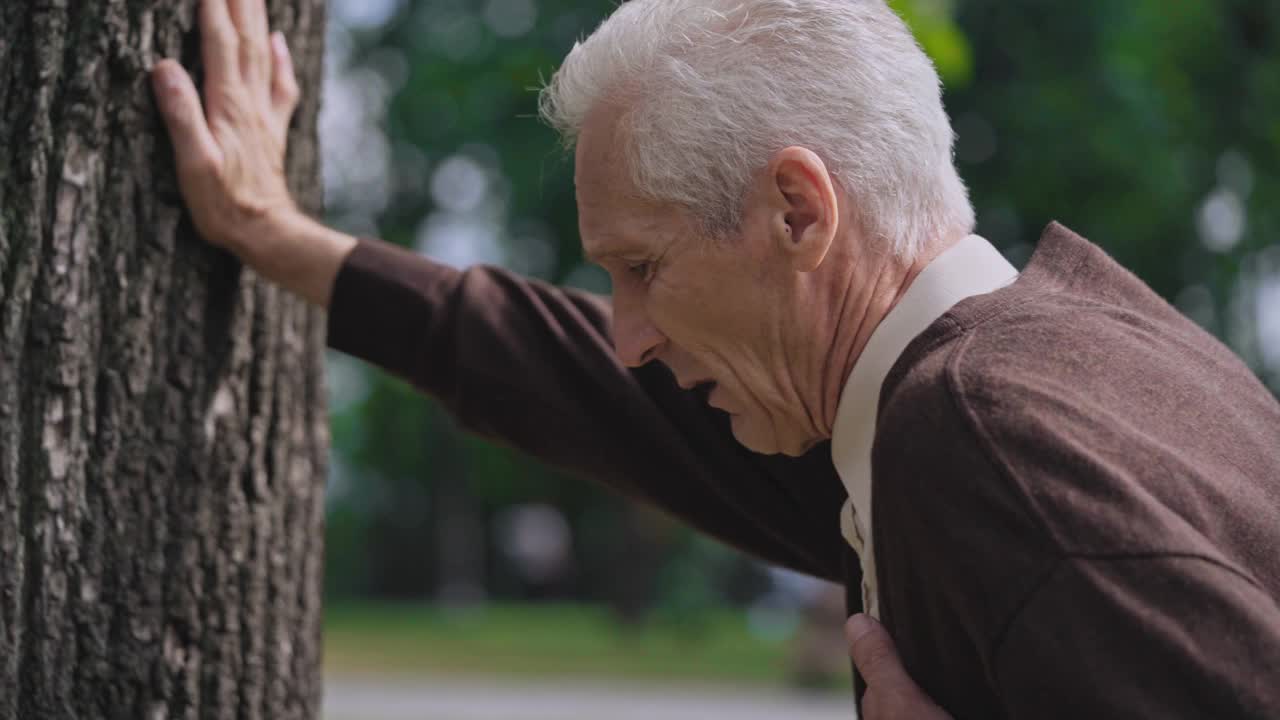 悲伤的成年男性心脏病发作，靠在树上，退休老人需要帮助视频素材