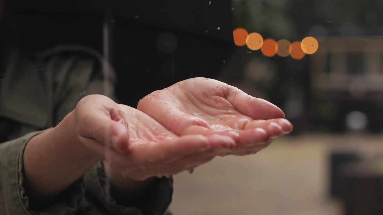 雨中，一位妇女站在伞下，雨水落在她的手掌上视频素材