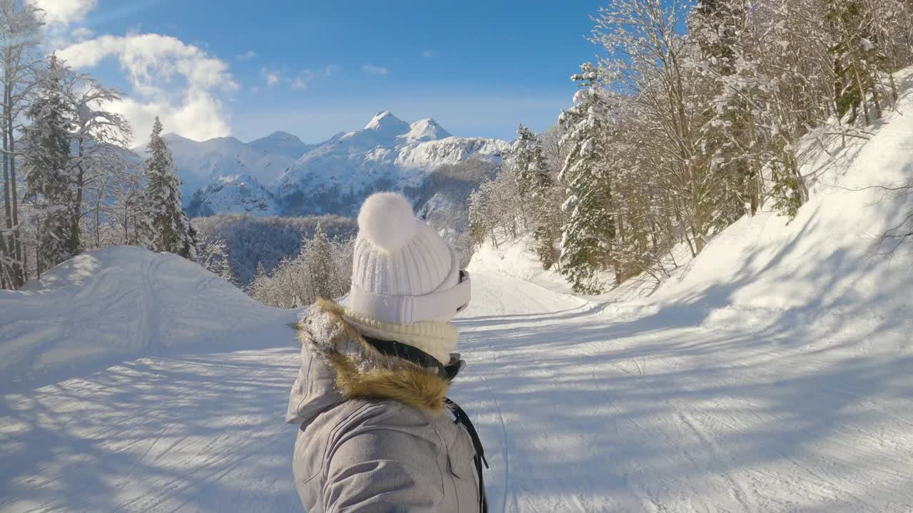 自拍:在一个阳光明媚的冬日，一名女子滑雪爱好者沿着整洁的斜坡滑行。视频素材