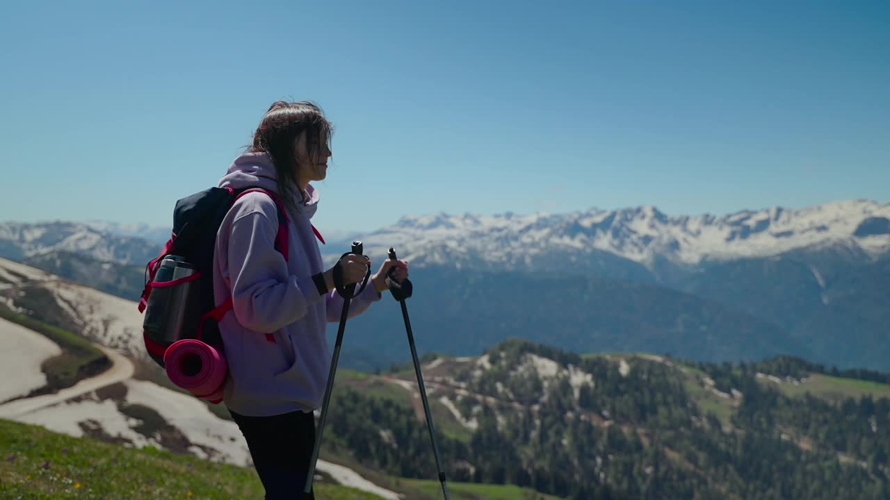 在山上徒步，年轻的女性徒步者背着背包和拐杖视频素材