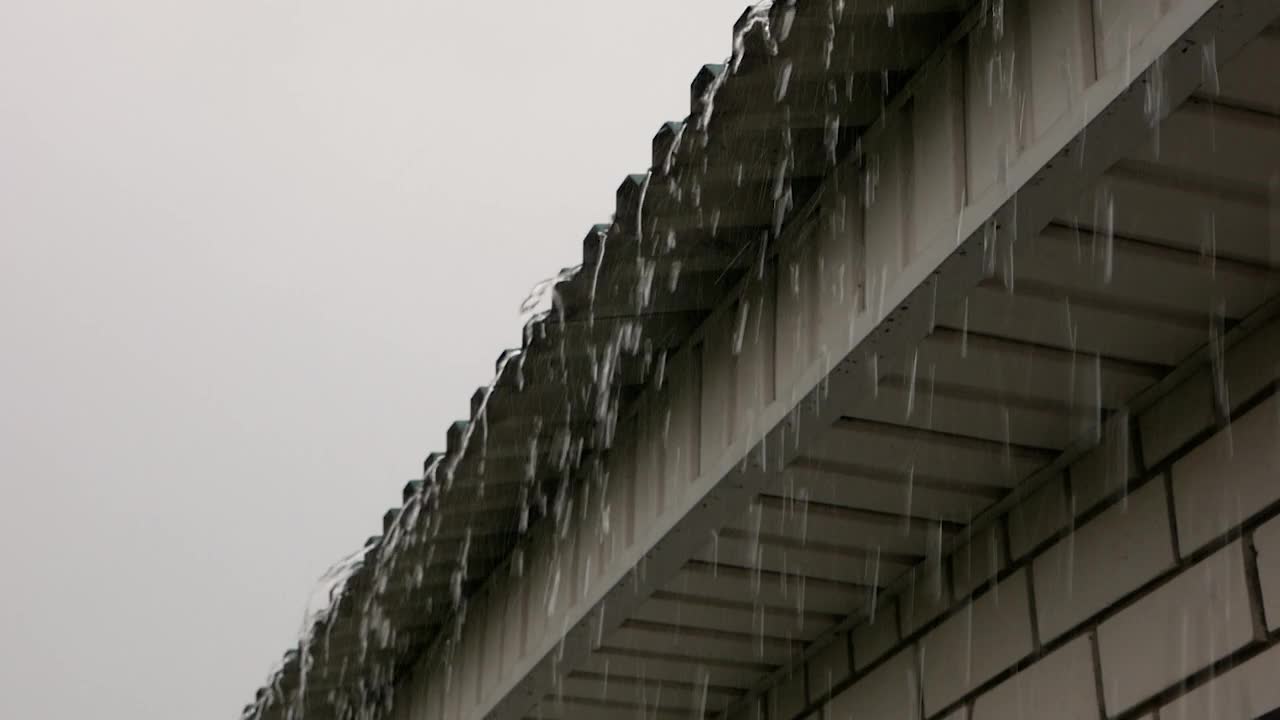 雨水如暴雨般从屋顶倾泻而下。雨季，全球气候变化。秋天的雪和糟糕的天气。大雨打在屋顶上。有选择性的重点视频素材