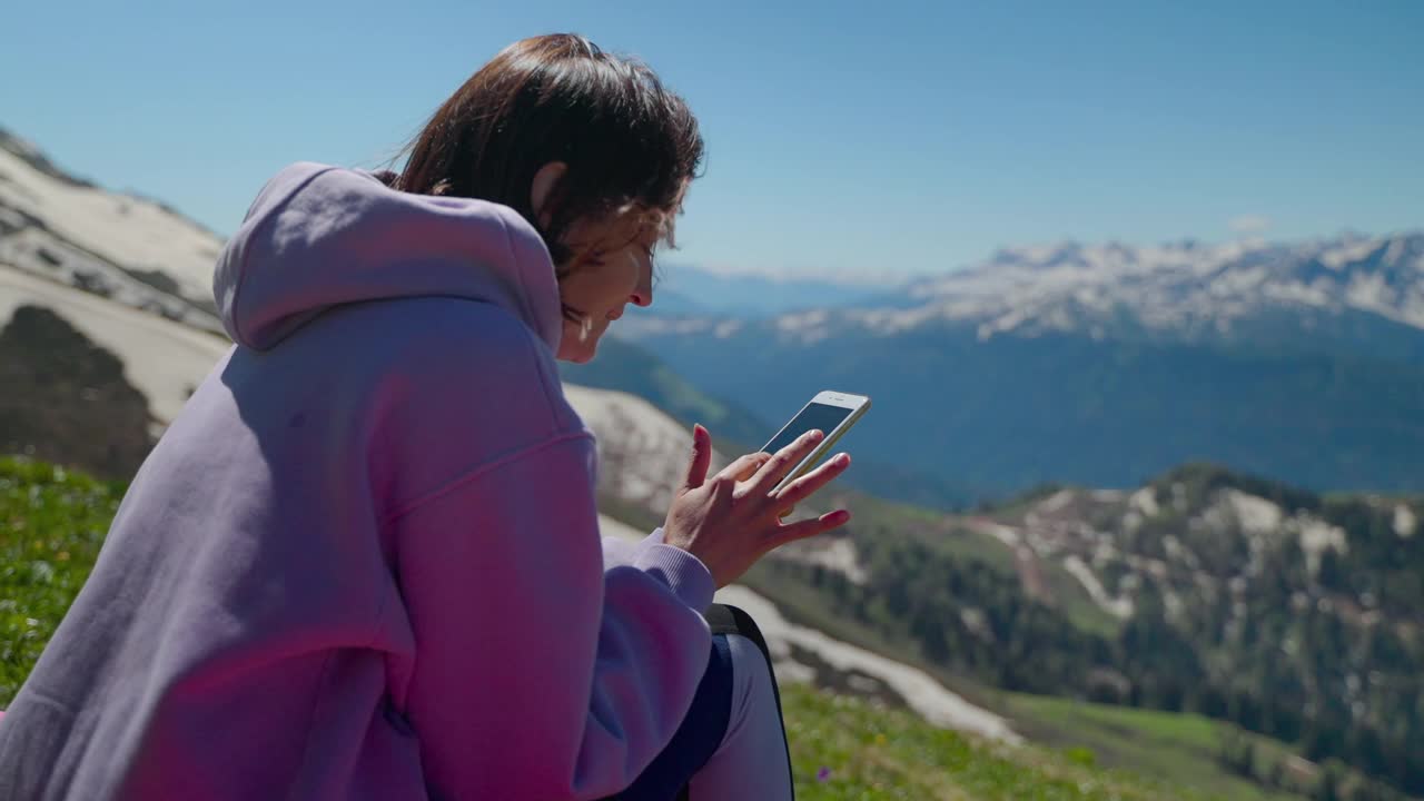 年轻的女驴友拿着手机站在山顶，快乐的驴友正在休息视频素材