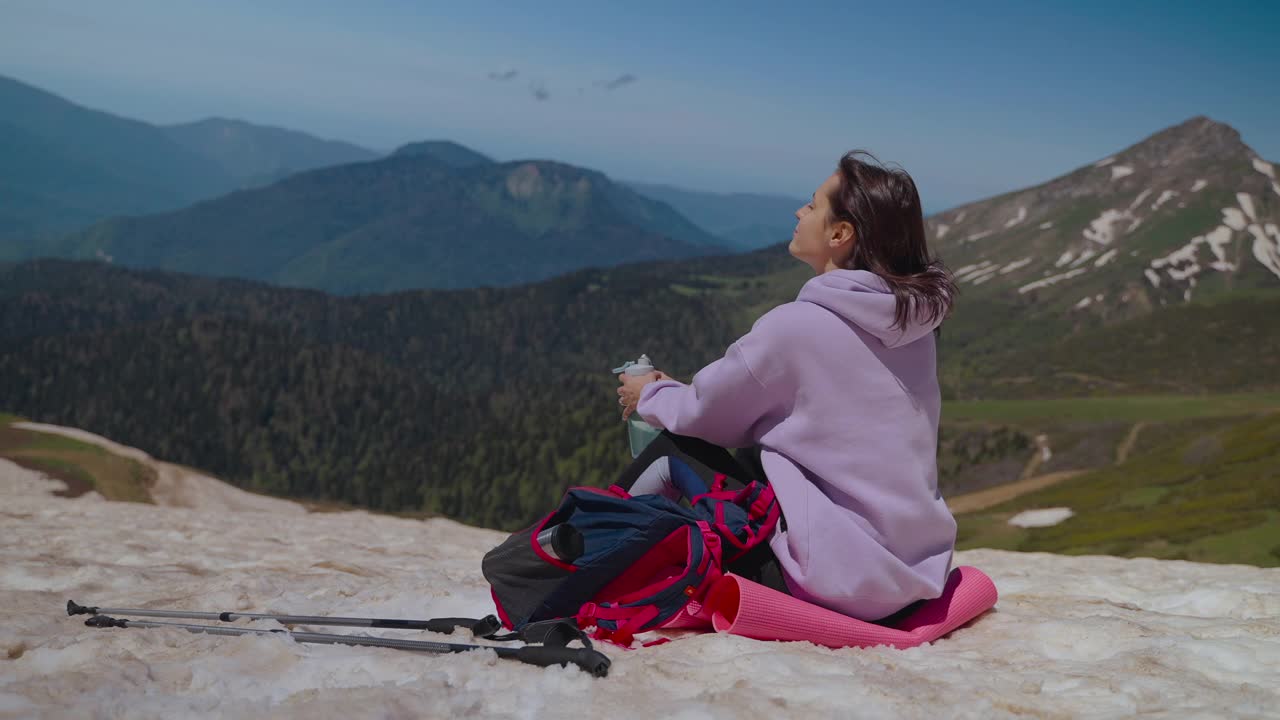 登山后，女游客在山顶休息，坐在雪地上欣赏大自然视频素材