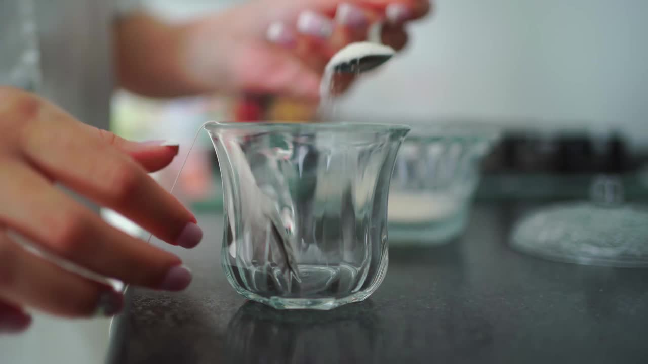 女人把糖和茶包放进杯子里，然后倒热水。酿造茶。视频素材