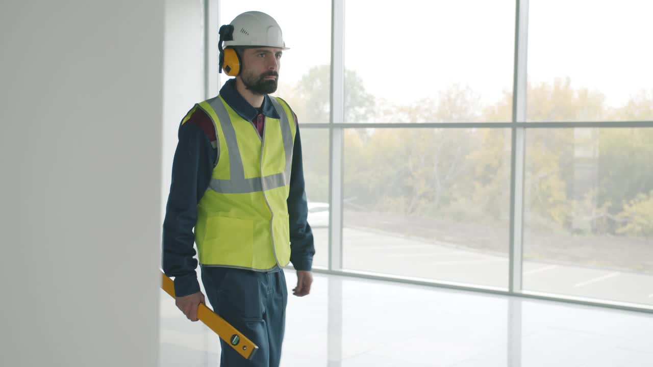 严肃的建筑工人穿着制服，拿着工具在空荡荡的办公中心里慢悠悠地走着视频素材