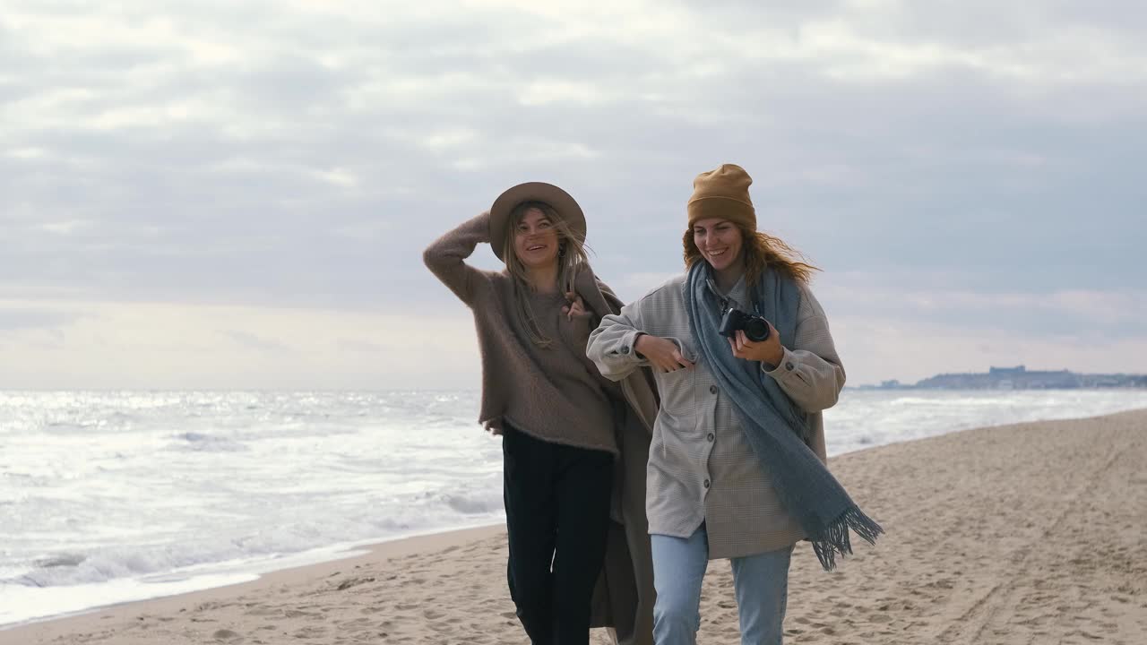 美丽的女孩在海边散步。在寒冷的阳光明媚的日子里，一对女性夫妇在海边玩得很开心视频素材