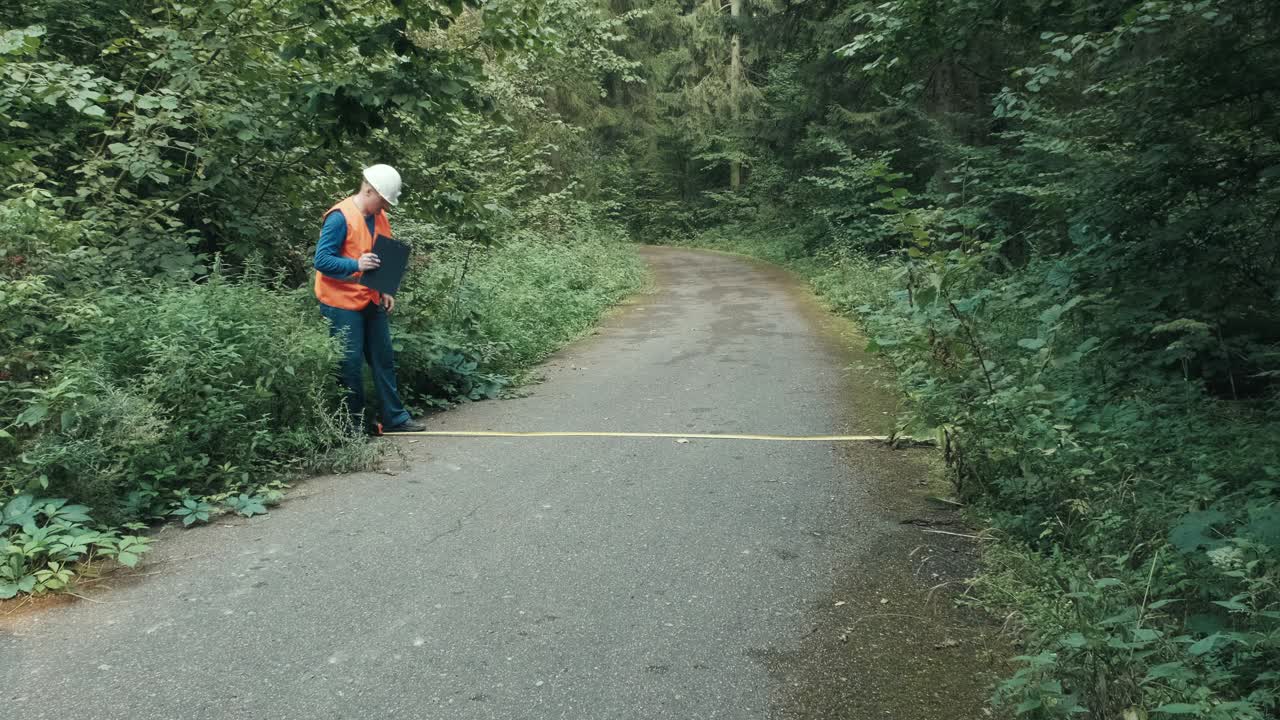 工人在工作服和在森林公路上用卷尺测量道路视频素材