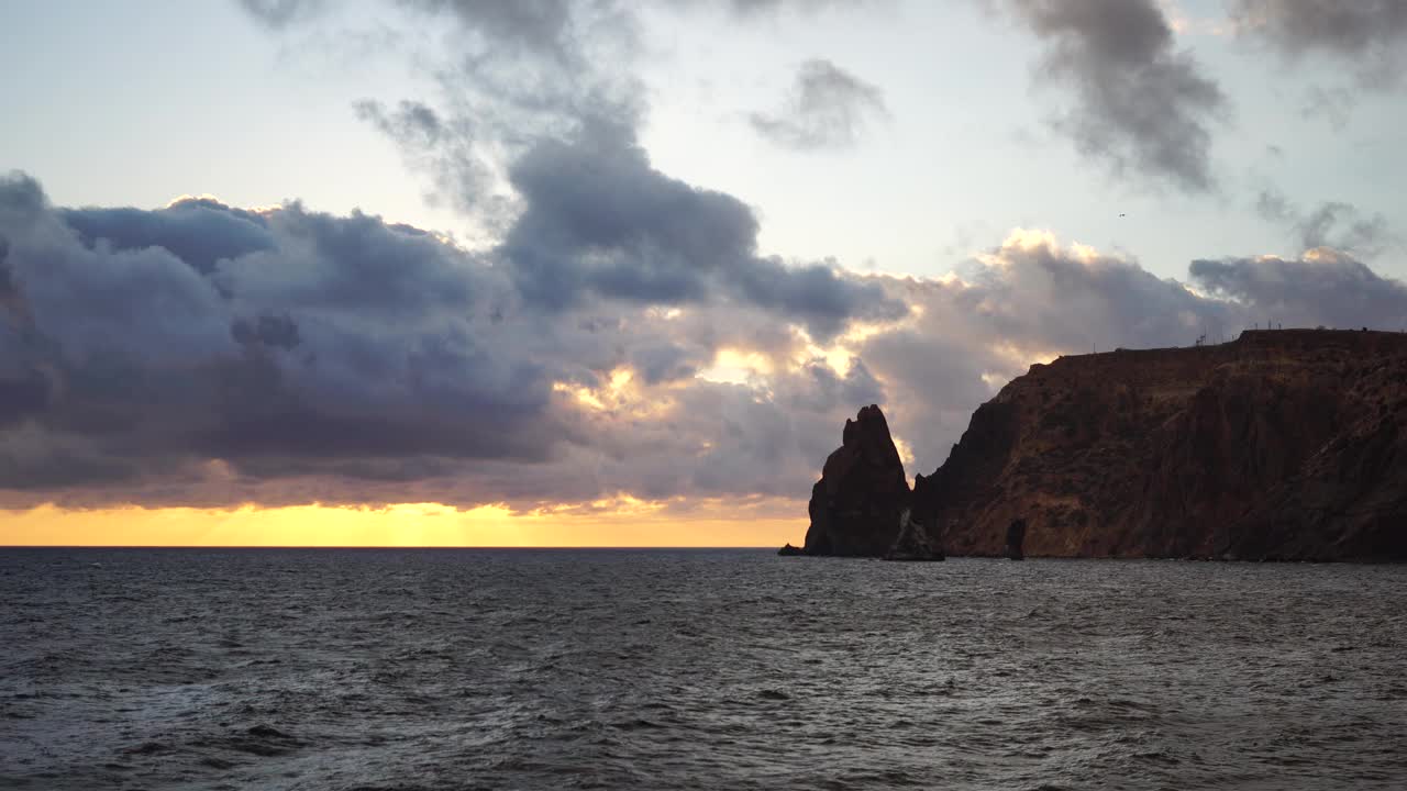 海洋和火山玄武岩上色彩斑斓的温暖日落，就像在冰岛。海浪撞击着岩石，被温暖的落日照亮，溅起白色的泡沫。永无止境的自然之美视频素材