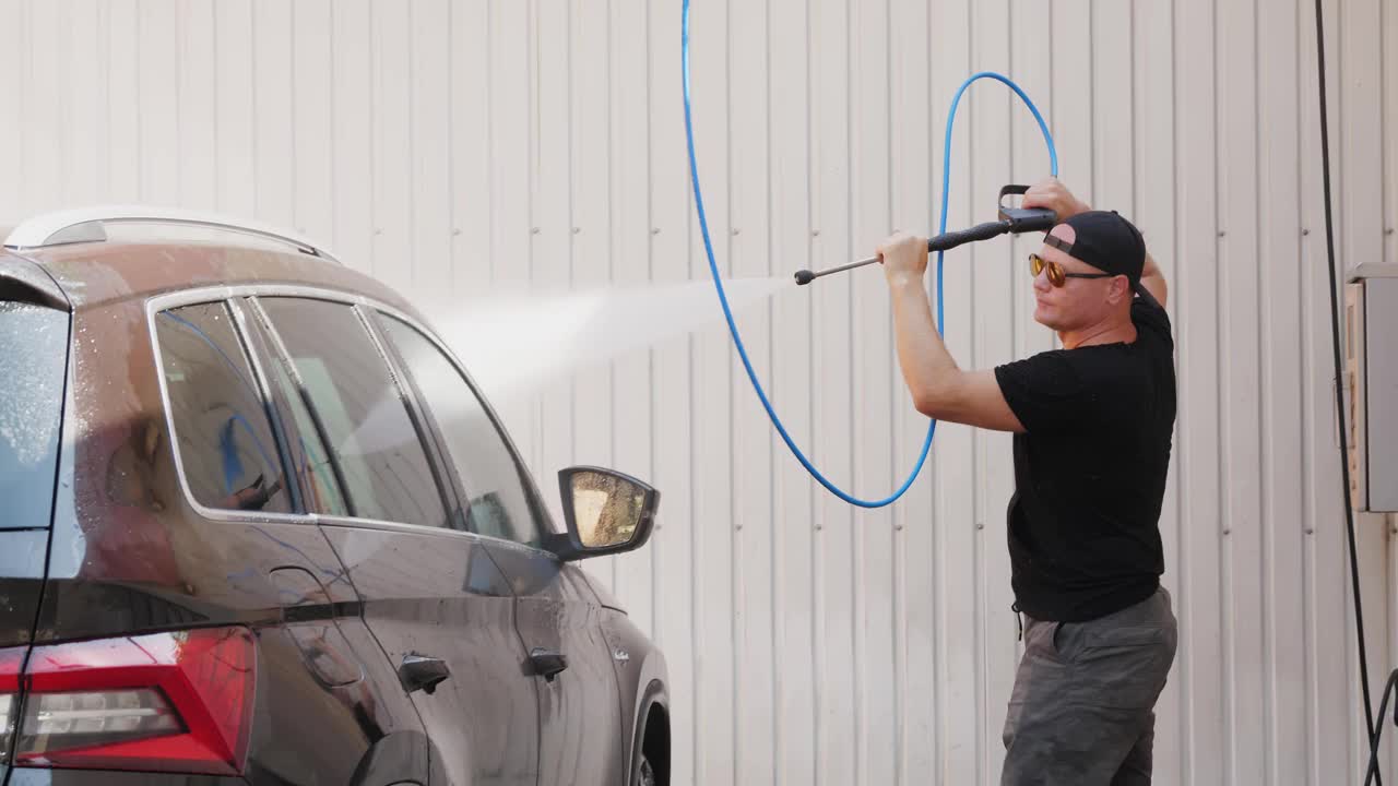 洗车。一名男子在自助洗车处用高压喷雾清洁汽车。汽车清洗视频素材