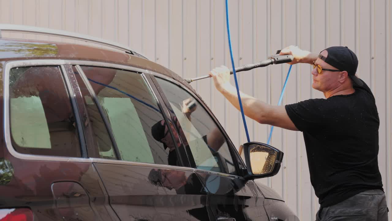 洗车。一名男子在自助洗车处用高压喷雾清洁汽车。汽车清洗视频素材