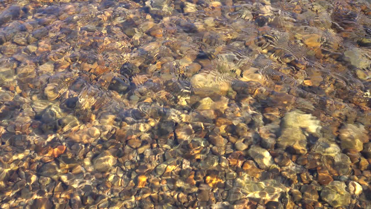 阳光照亮了卵石底和波纹表面的浅山河流，背景视频素材