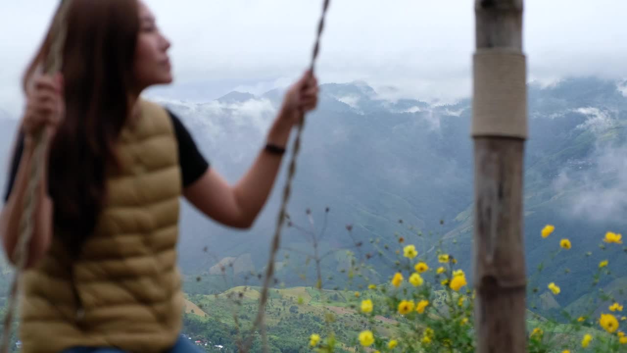 模糊的一个女人坐在一个秋千与一个美丽的山景在阴天视频素材