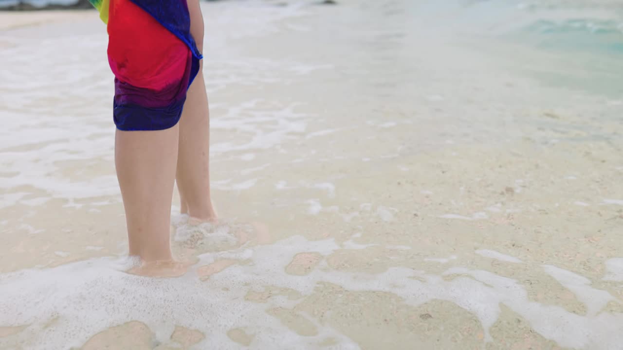 女腿部分穿着彩虹沙滩裙享受在热带沙滩踢海浪，清澈的海水，轻松夏日热带天堂岛海滩度假，海浪打脚视频素材