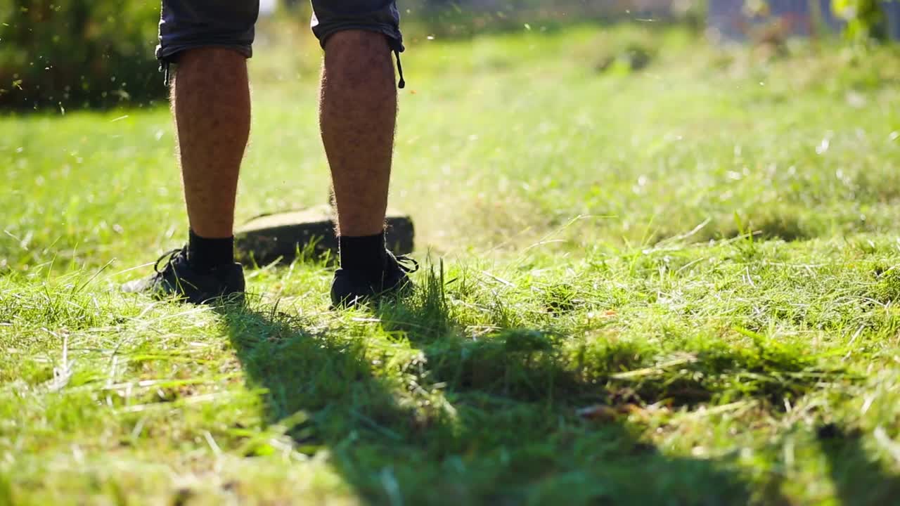 一个男人在院子里的草坪上用修剪机割草。在郊区和农村地区的庭院护理。视频素材