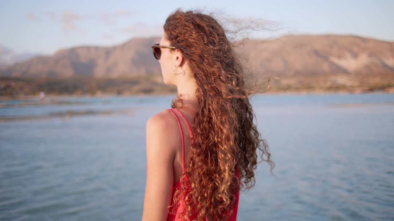 日落时分，一名30多岁身穿红色连身衣的女子在泻湖浅水中。视频素材