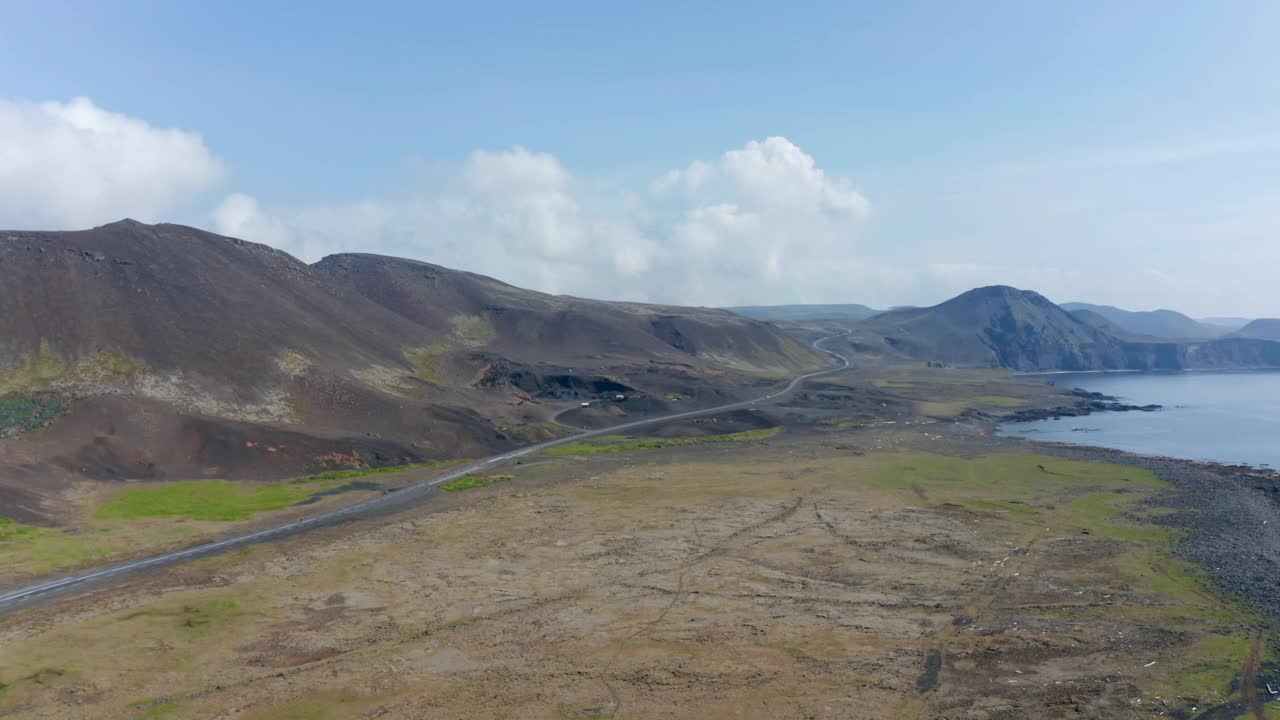 鸟瞰冰岛的海岸线与火山黑沙滩和环形公路公路。无人机反向飞行显示了一些农用机械视频素材