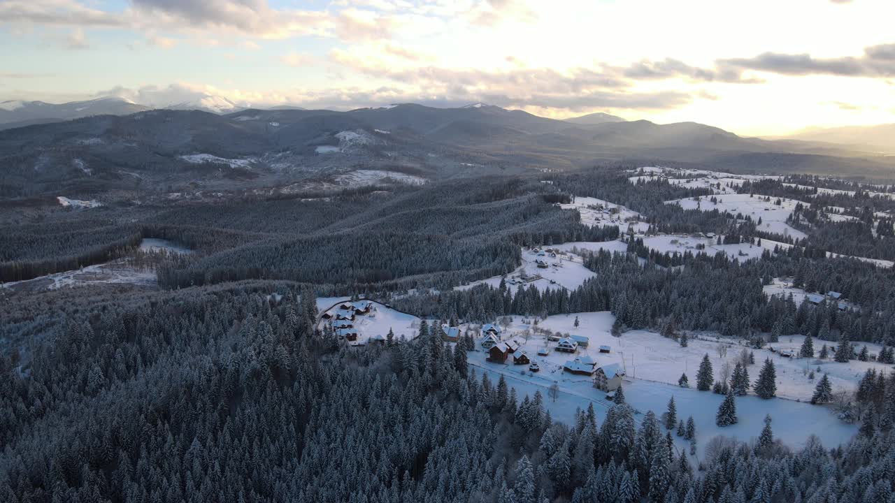 空中冬季景观与小村庄房屋之间的雪覆盖森林在寒冷的山在晚上视频素材