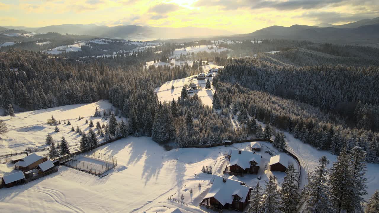 空中冬季景观与小村庄房屋之间的雪覆盖森林在寒冷的山在晚上视频素材