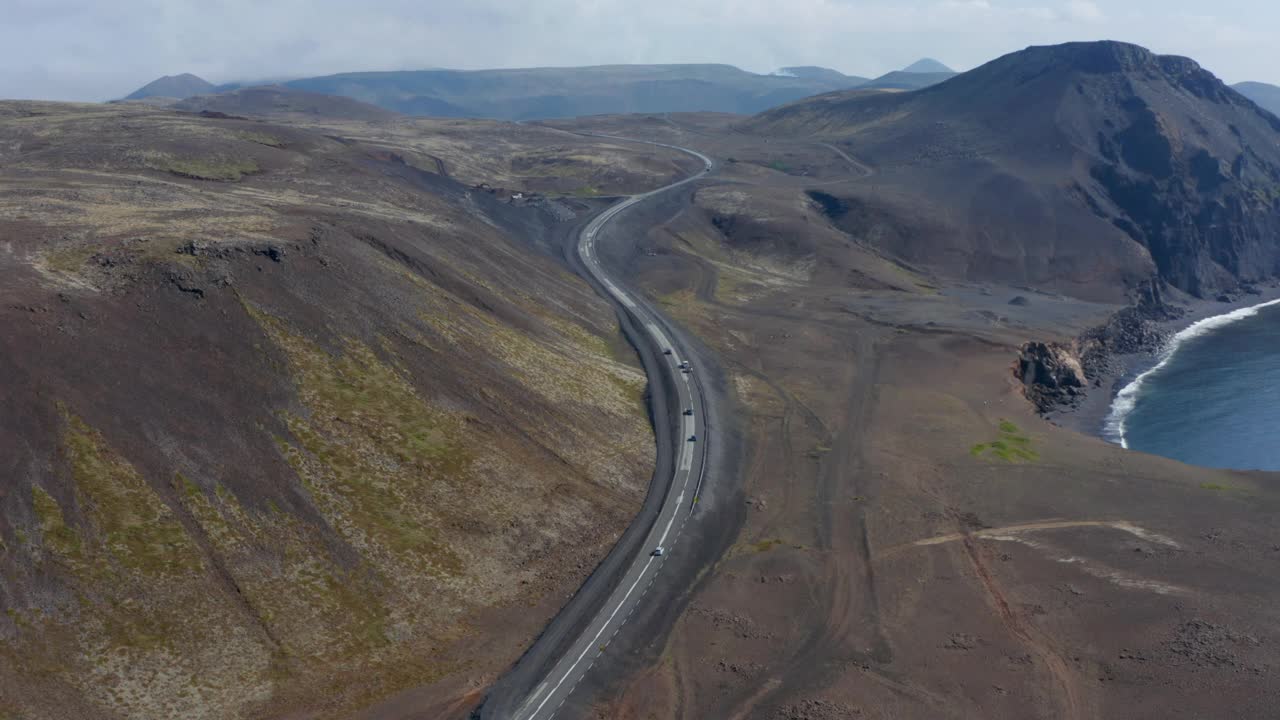 鸟瞰图轻轻地旋转在环城公路上，汽车平静地行驶在冰岛的火山景观。无人机拍摄的冰岛海岸线上的黑色沙滩视频素材